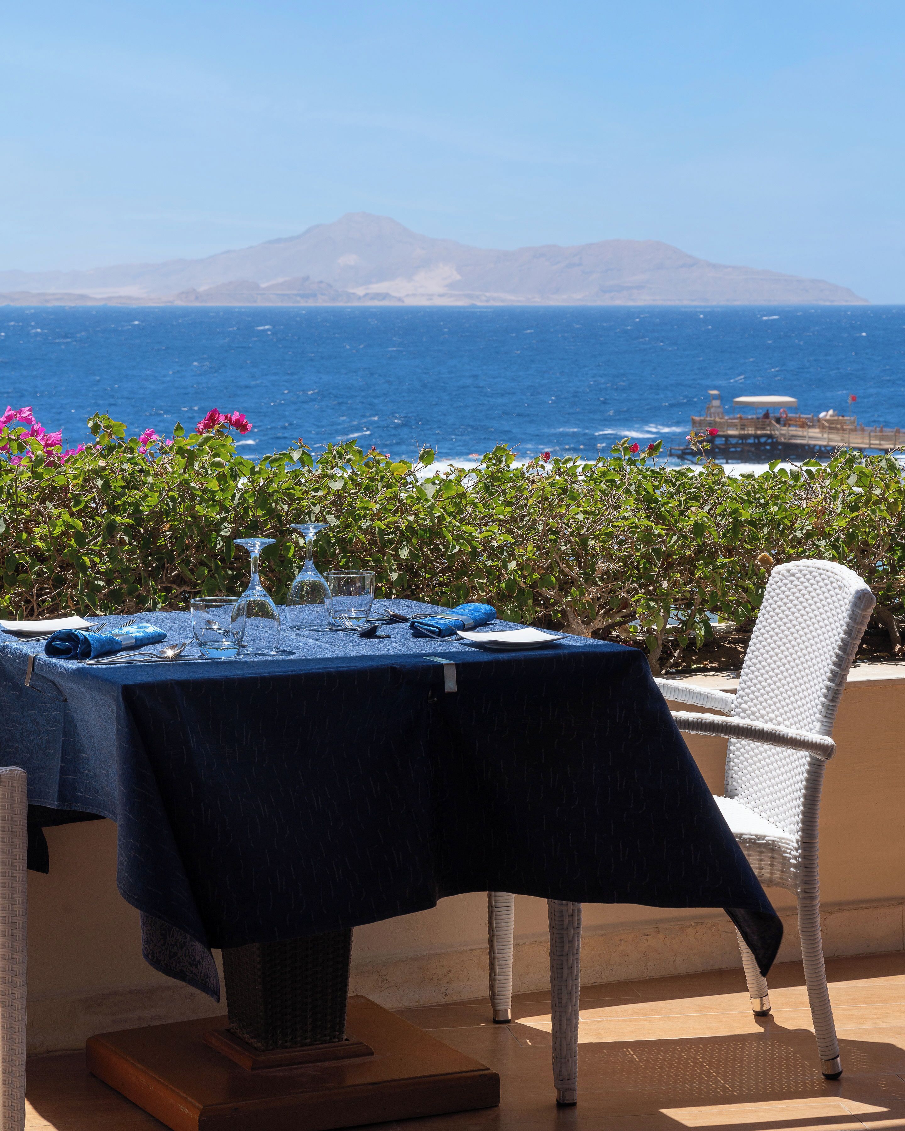 Une table dressée pour deux personnes, avec vue sur l’océan et les montagnes en arrière-plan.