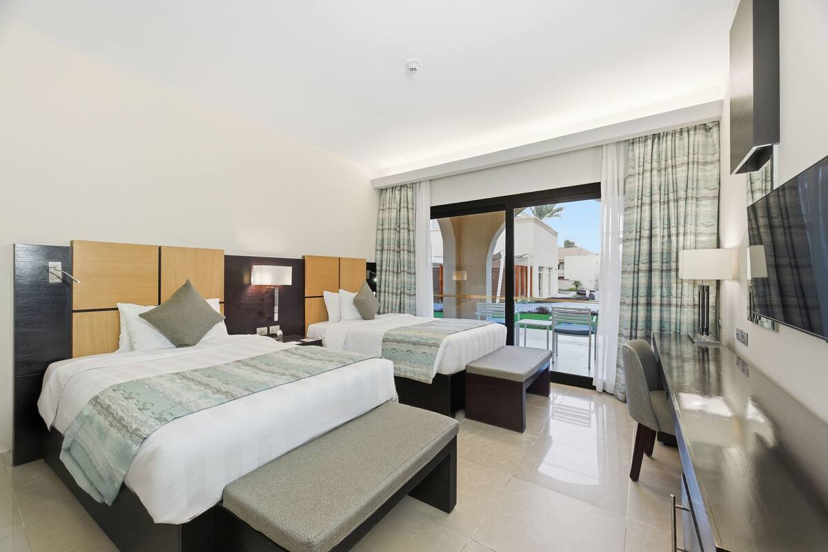 Une chambre d’hôtel avec deux lits, un banc, un bureau, une télévision et une vue sur une piscine.