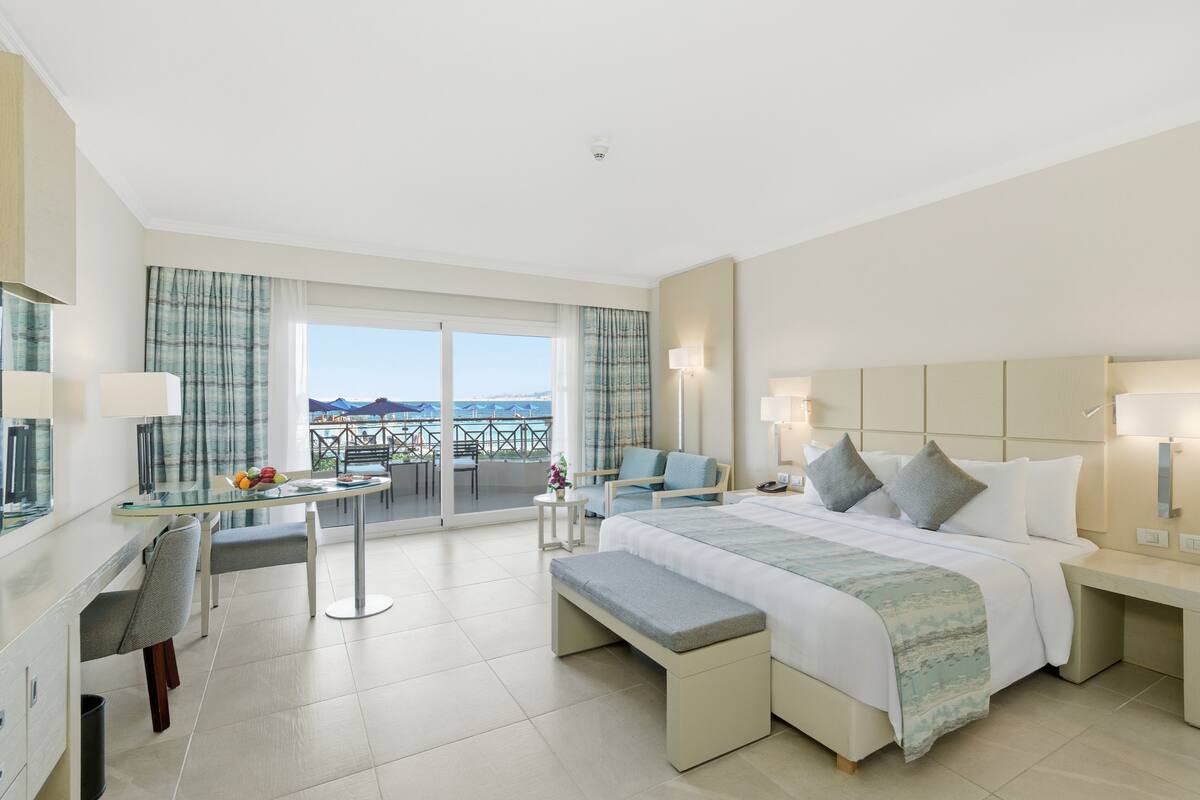 Une chambre d’hôtel équipée d’un lit, d’un bureau, d’une chaise, d’un banc et d’un balcon avec vue.