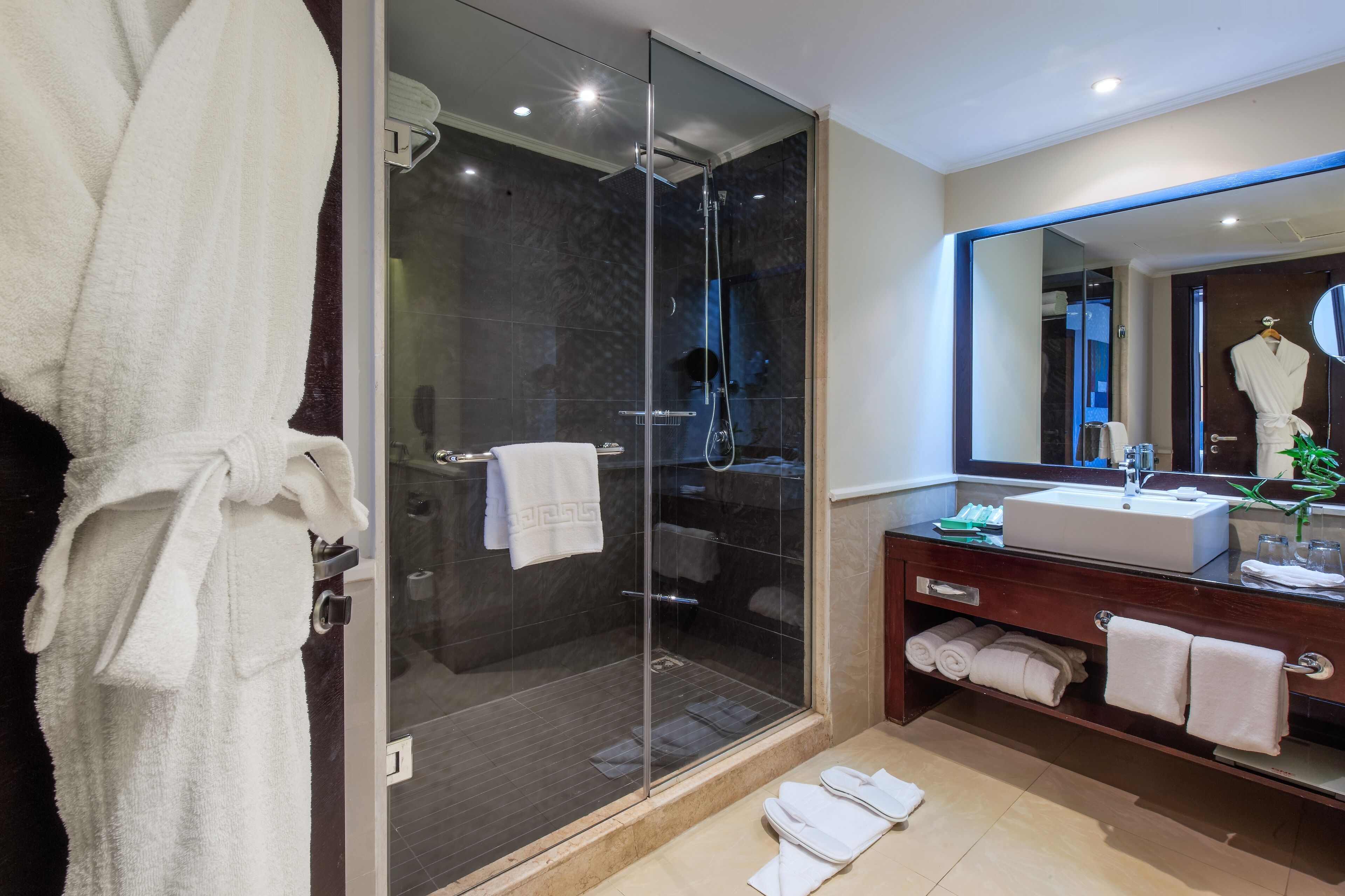 Un baño moderno con ducha envuelta en vidrio, tocador con espejo y toallas ordenadas.