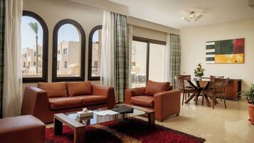 A modern living room with a brown leather sofa, a coffee table, and a dining area with wooden chairs and a glass table.