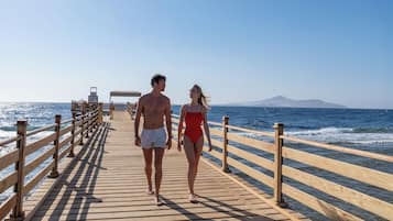 A wooden pier extending into the sea with a clear sky and distant mountains.