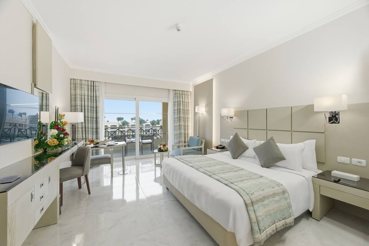Une chambre d’hôtel dotée d’un grand lit, d’un bureau avec un téléviseur à écran plat, d’un balcon avec une table et des chaises, et offrant une vue sur l’extérieur.