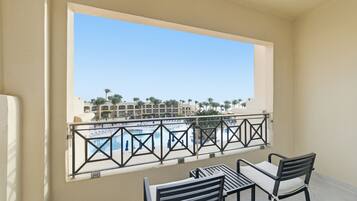 A balcony with a view of a pool and palm trees, a table with chairs, and a railing.