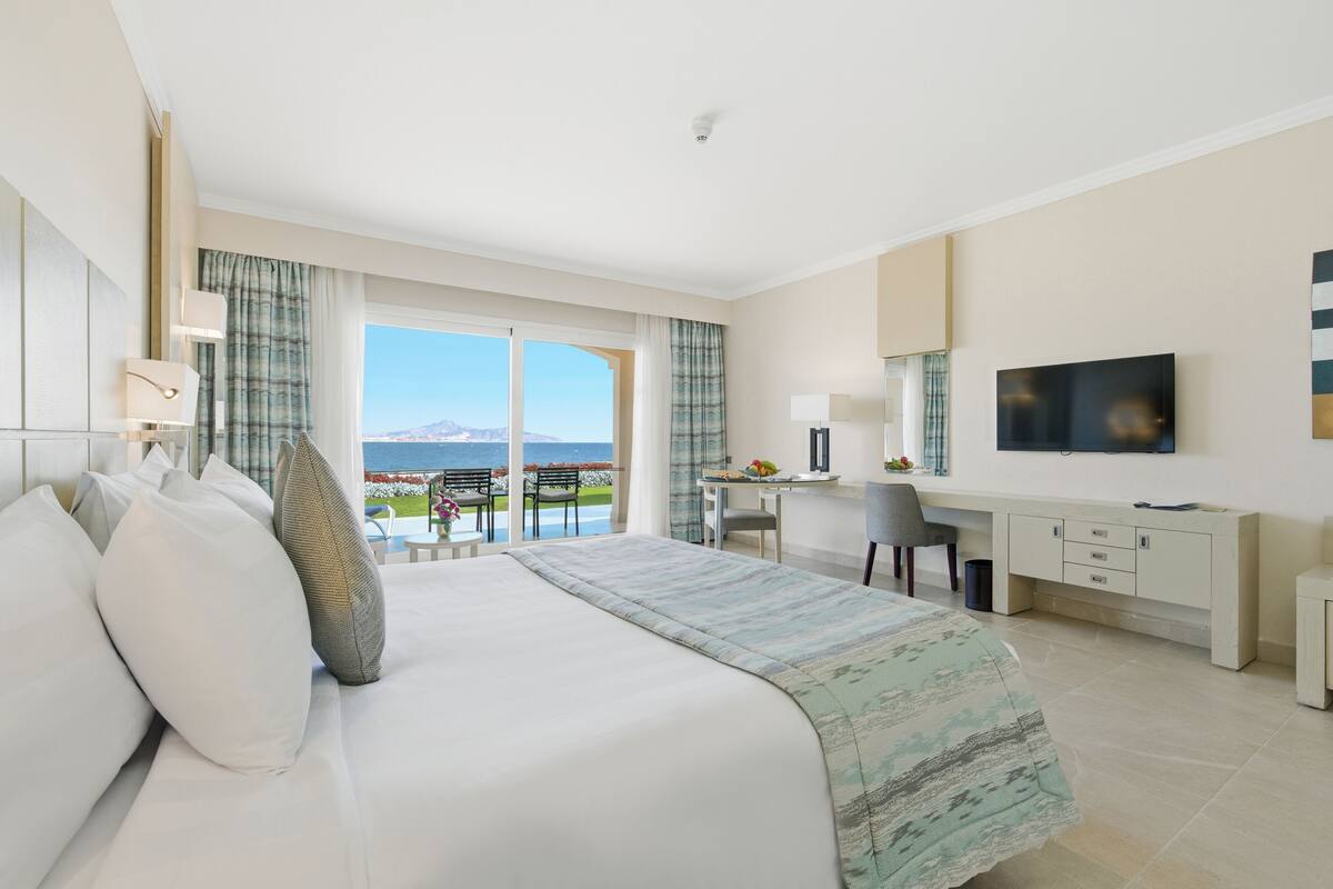 Une chambre d’hôtel avec un lit, un bureau, une télévision et une vue sur la mer.