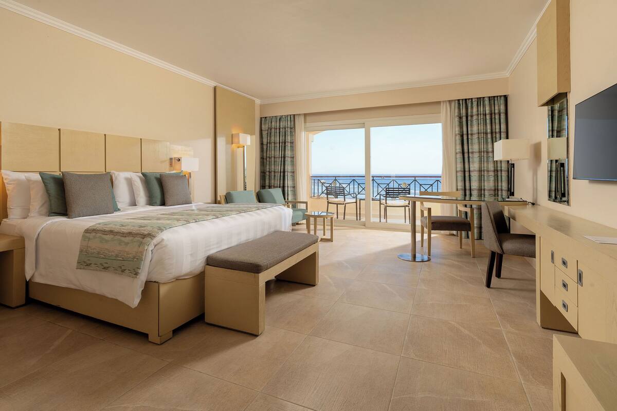 Une chambre d’hôtel comprenant un lit, une banquette, un bureau et un balcon avec vue sur la mer.