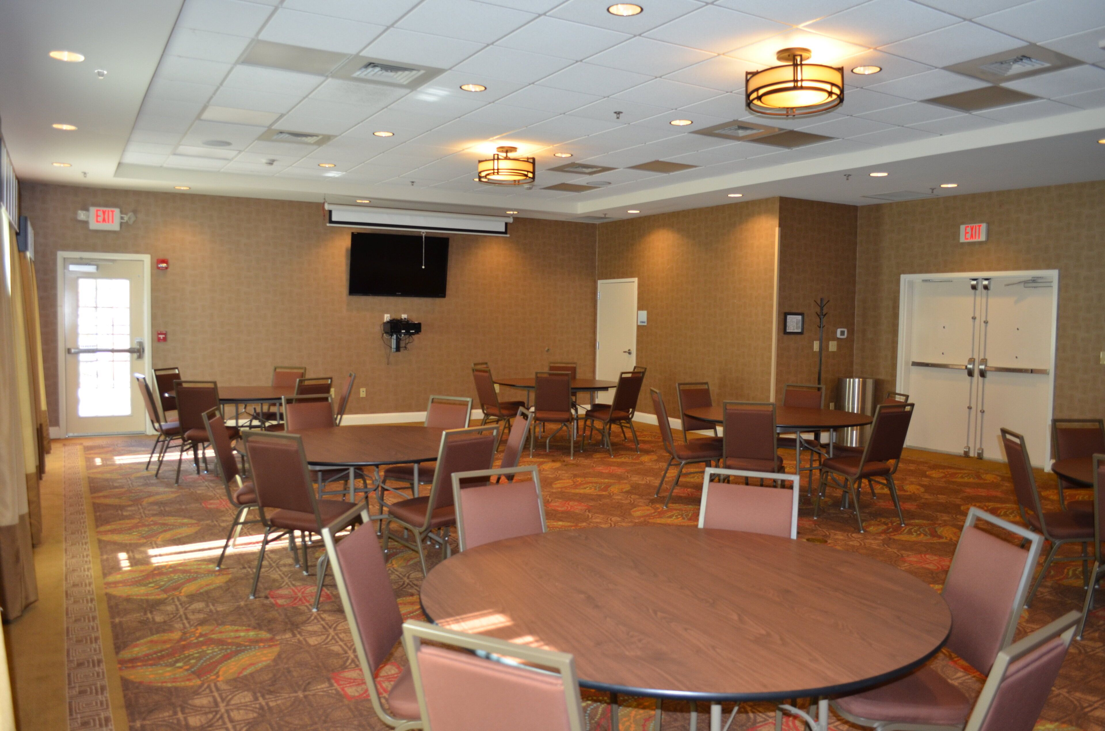 A conference room with multiple tables and chairs, a flat-screen TV mounted on the wall, and an exit sign.