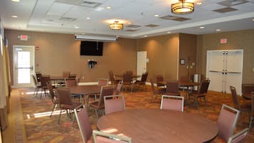 A conference room with multiple tables and chairs, a flat-screen TV mounted on the wall, and an exit sign.