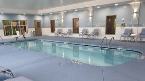 Un espace piscine comprenant une piscine à eau claire, des chaises longues et un espace d’attente avec des chaises et un banc.
