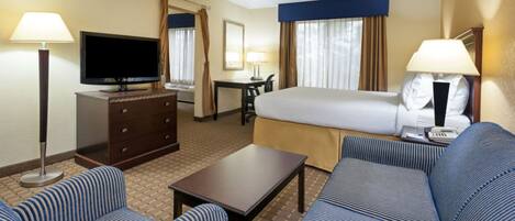 A hotel room with a bed, a TV, a desk, a chair, a sofa, and a lamp.