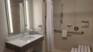 Un baño moderno con un espejo grande, un lavamanos blanco, una ducha con cabezal de ducha manual y una barra de apoyo.