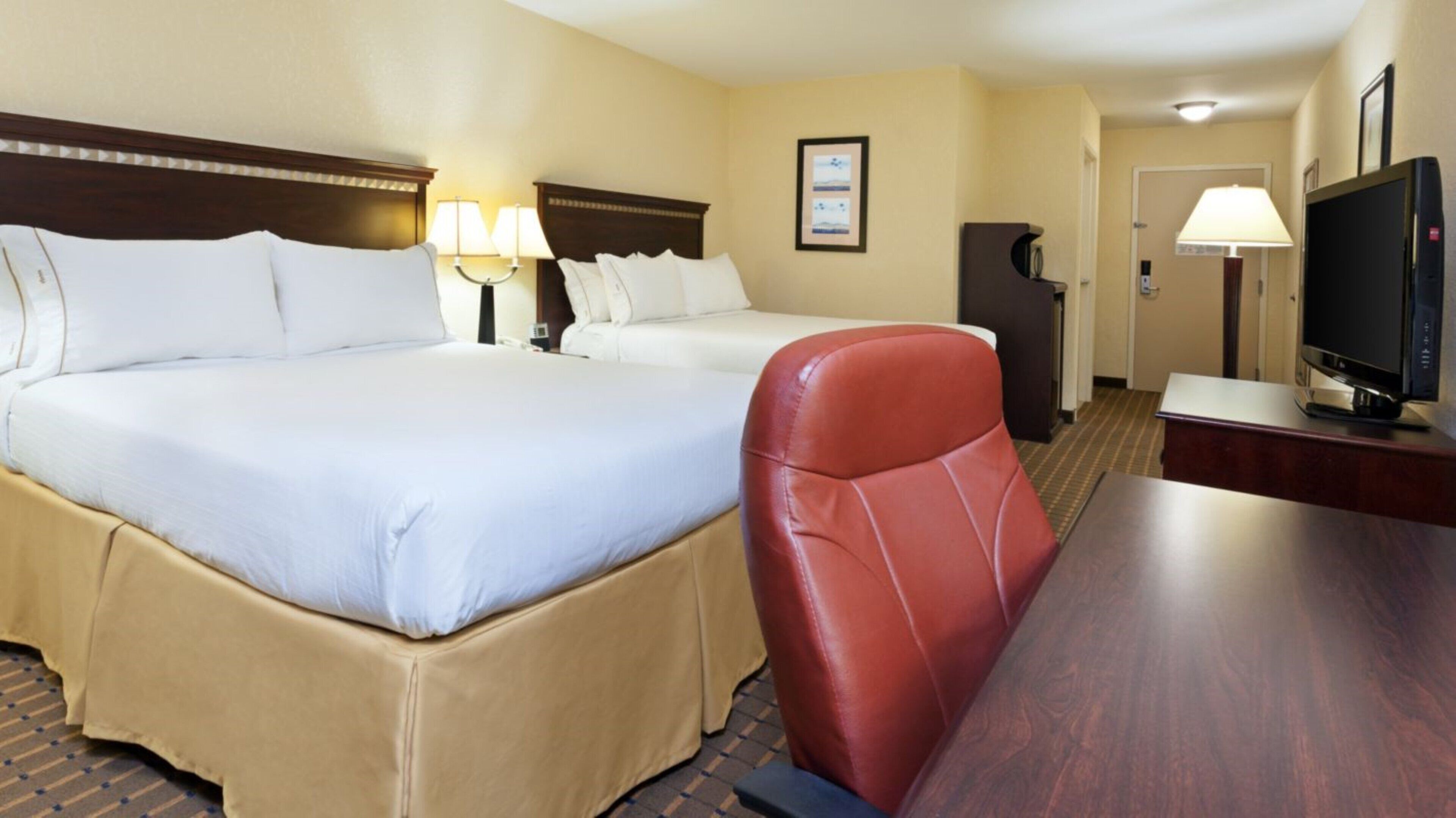 A hotel room with two beds, a desk, a television, and a chair.