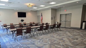 Une salle de conférence avec une longue table, des chaises, un téléviseur à écran plat, un drapeau américain et une moquette à motifs.