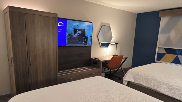 Une chambre d’hôtel avec deux lits, un bureau avec une chaise, un téléviseur fixé au mur et une armoire.
