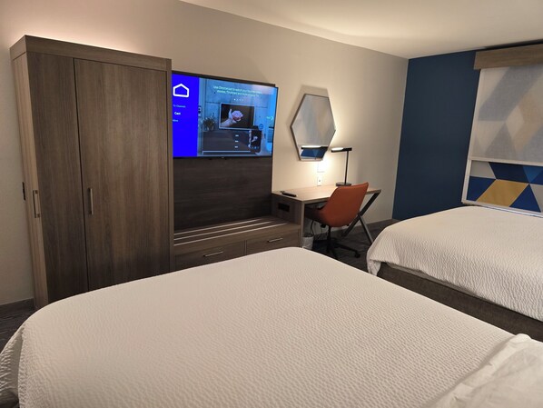 A hotel room with two beds, a desk with a chair, a TV mounted on the wall, and a wardrobe.