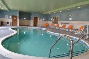Una piscina interior de borde curvo, rodeada de sillones de descanso y una zona junto a la piscina.