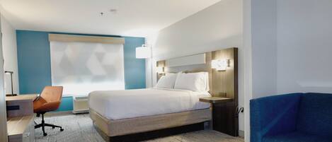 Una habitación de hotel con cama, escritorio con silla, sofá azul y un ventanal grande.