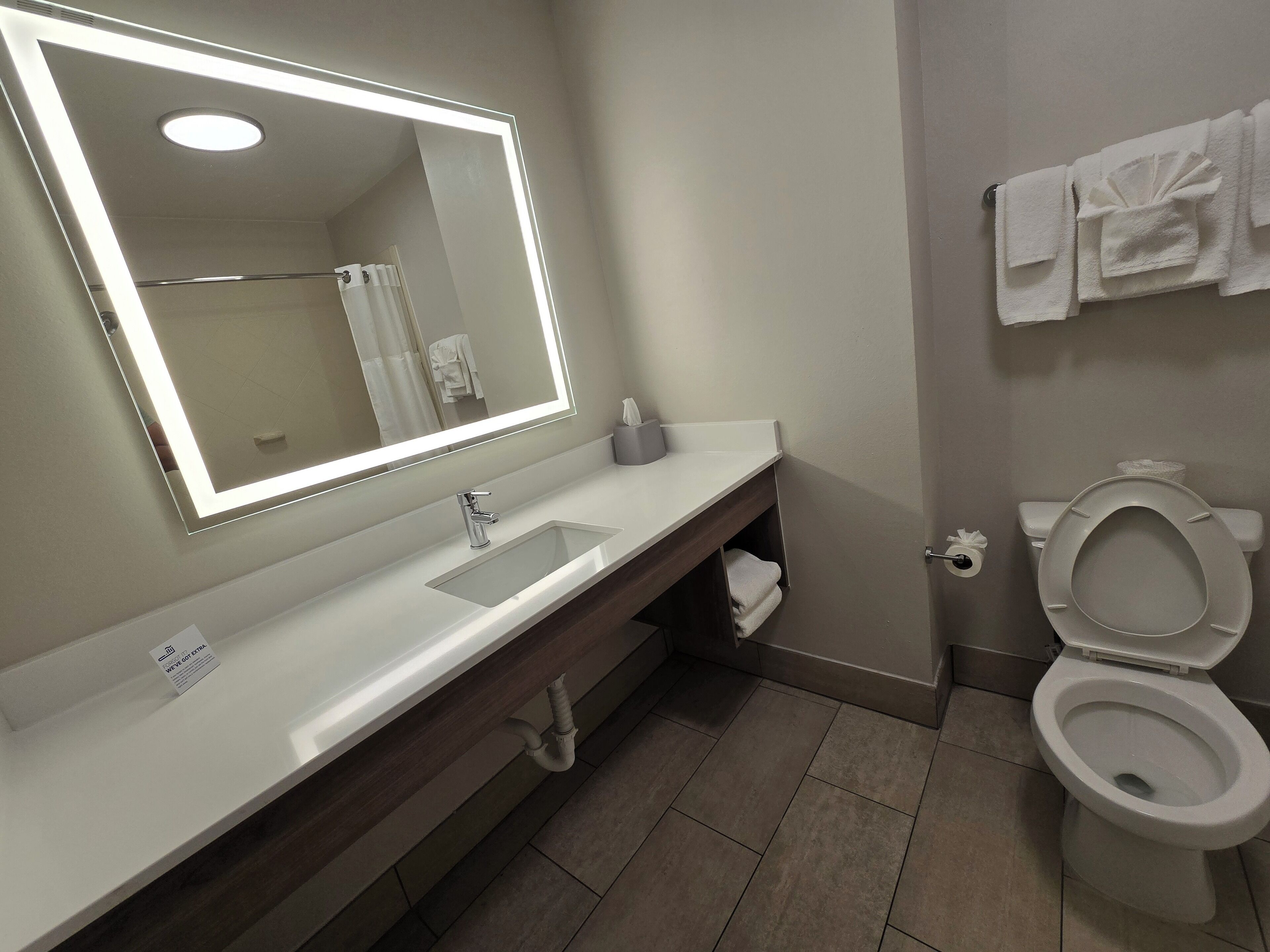 A modern bathroom with a large mirror, white sink, and toilet.