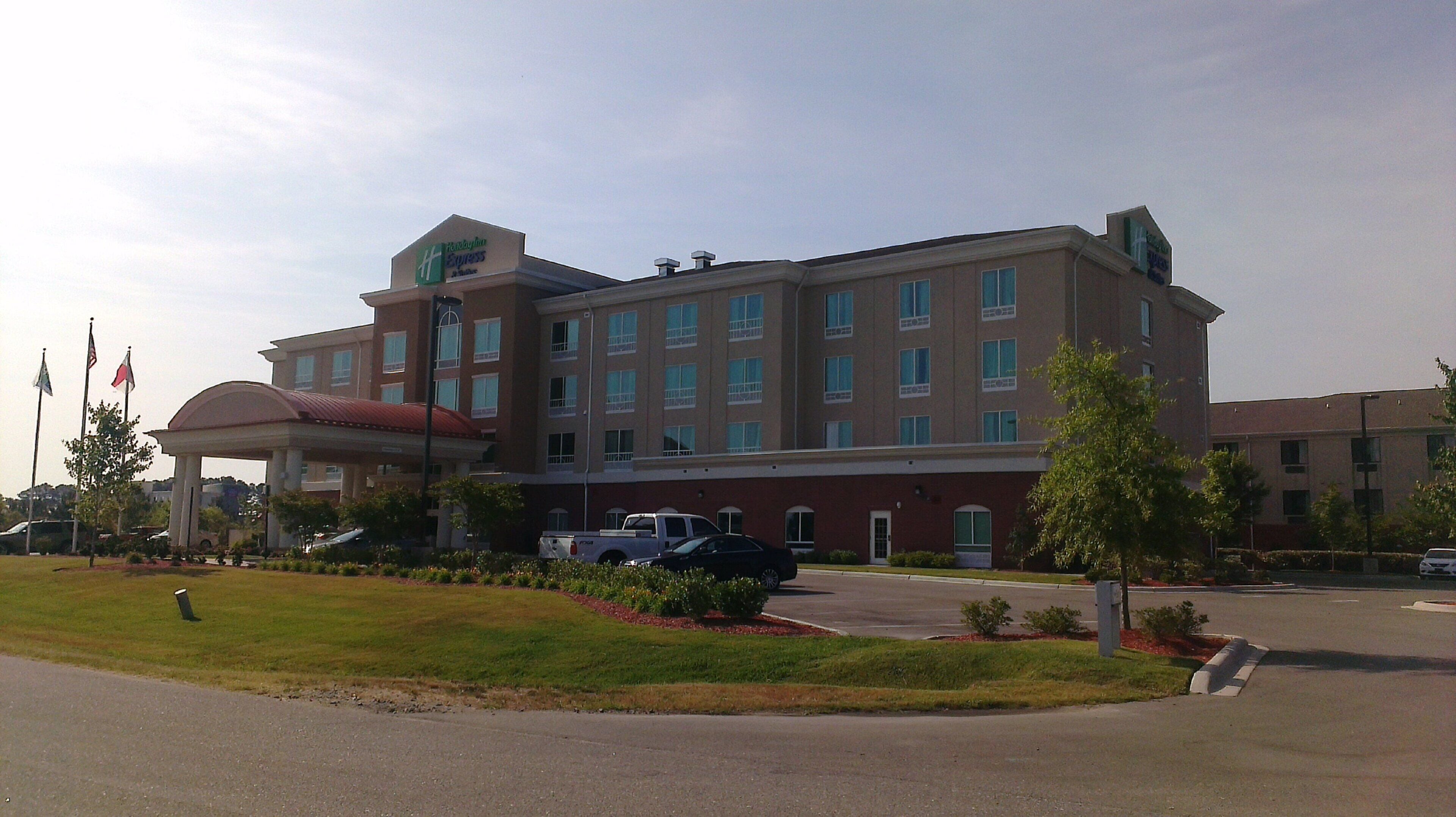 A multi-story hotel with a central entrance, a parking area, and a landscaped front yard.
