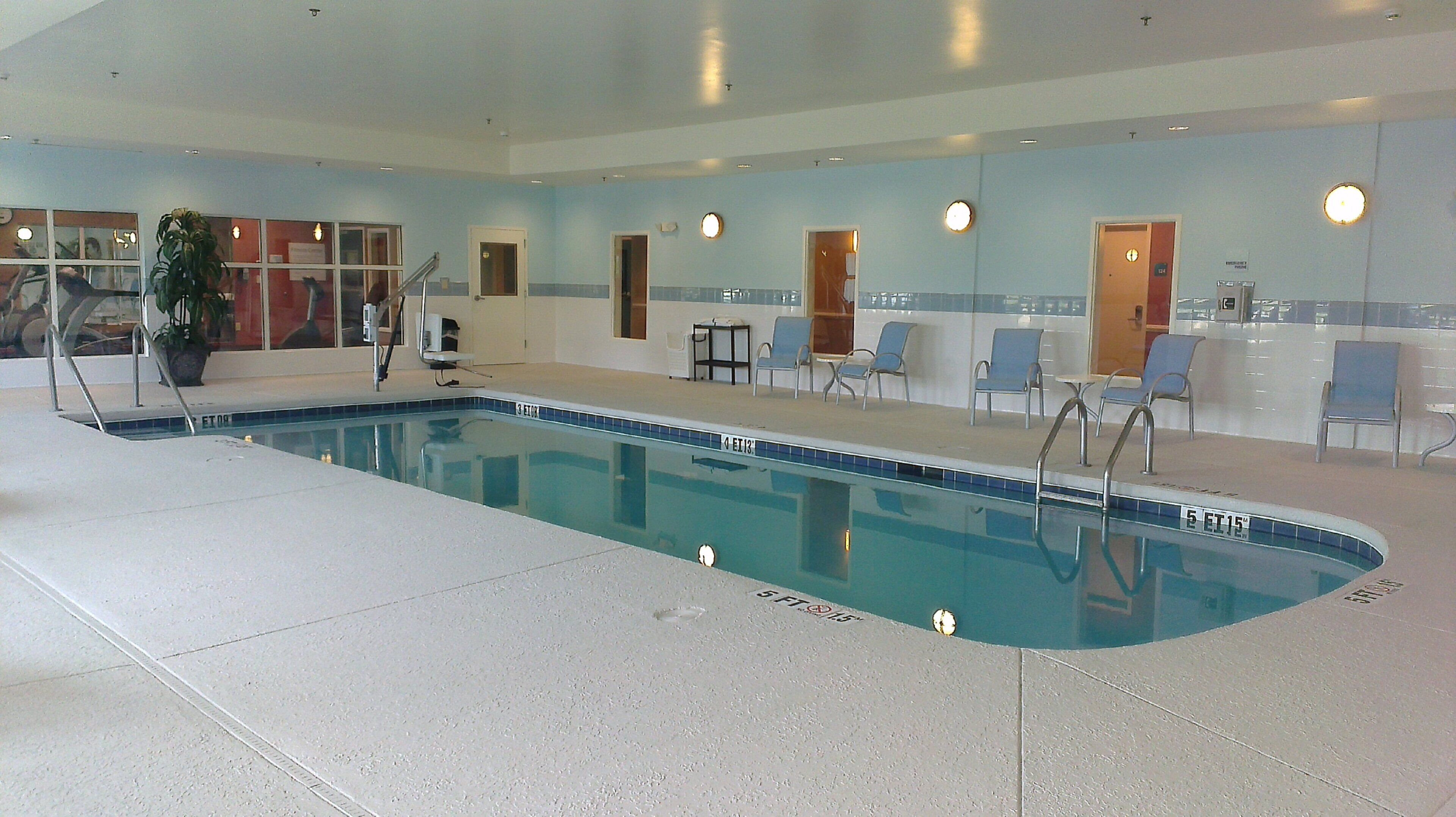 An indoor swimming pool with a tiled edge, lounge chairs, and a potted plant.