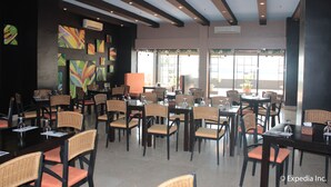 A restaurant with multiple tables and chairs, large windows, and colorful artwork on the walls. - Pamulinawen Hotel (San Nicolas)