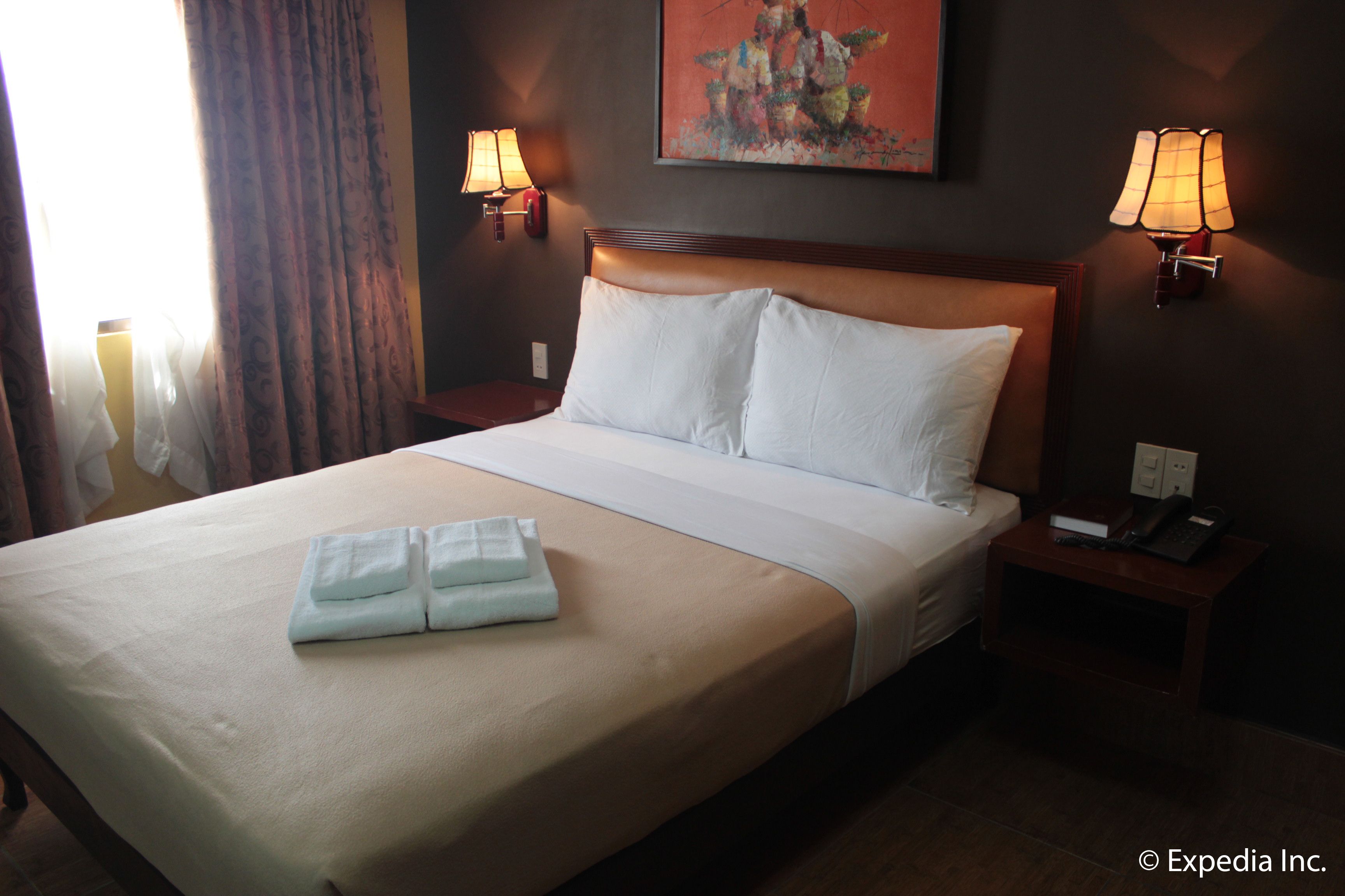 A hotel room with a large bed, two bedside lamps, a painting on the wall, and a telephone on the nightstand.