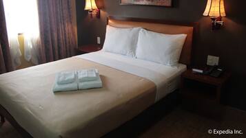 A hotel room with a large bed, two bedside lamps, a painting on the wall, and a telephone on the nightstand.
