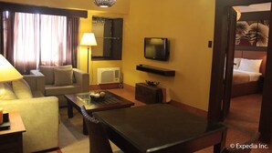 A hotel room with a sofa, a coffee table, a TV, a lamp, a mirror, and a bed. - Pamulinawen Hotel (San Nicolas)