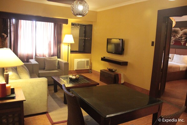 A hotel room with a sofa, a coffee table, a TV, and a bed. - Pamulinawen Hotel (San Nicolas)