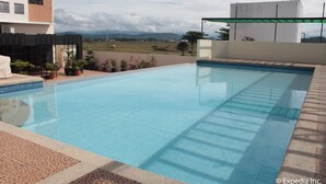 A swimming pool with clear blue water, surrounded by a tiled deck and potted plants. - Pamulinawen Hotel (San Nicolas)