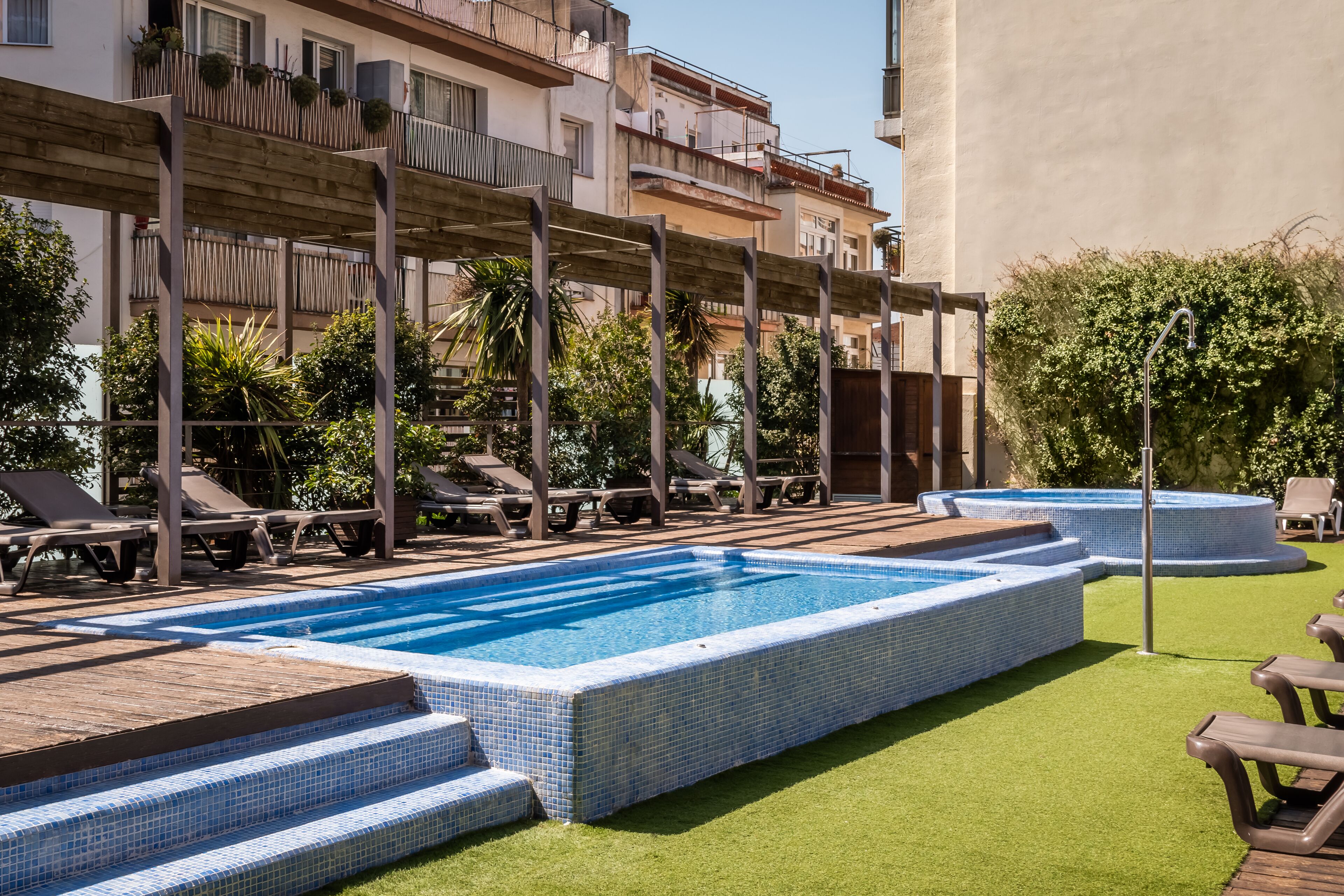 A swimming pool with tiled steps, lounge chairs, and a wooden deck.