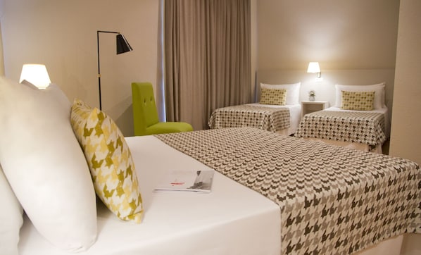 Habitación de hotel con dos camas, una silla verde y una lámpara.