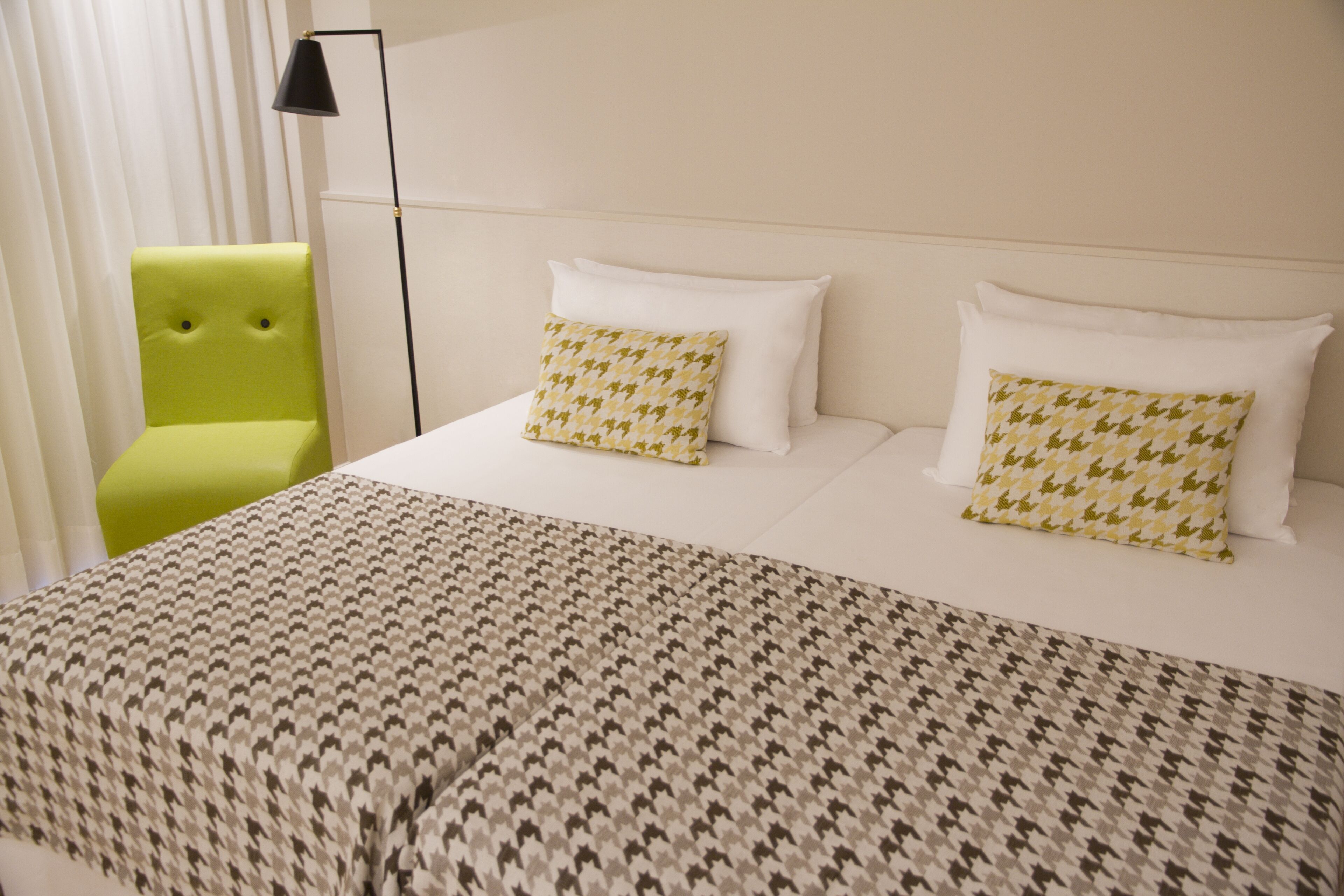 Una habitación de hotel con una cama, dos almohadas, una silla verde y una lámpara de pie.