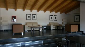A modern living room with a high ceiling, built-in wooden beams, and a stone floor. There are two sofas, a coffee table, and a small table with a lamp.