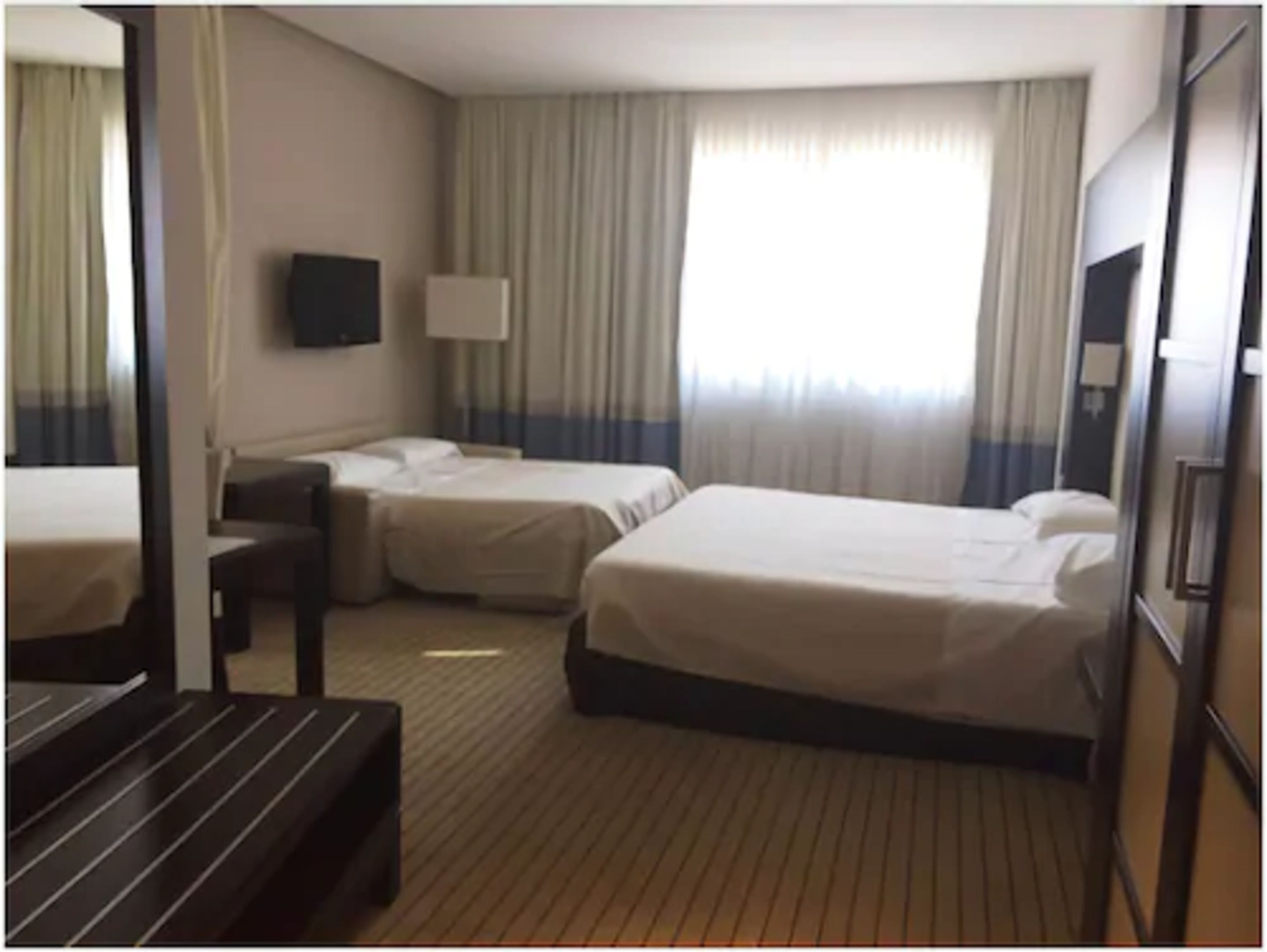 Una habitación de hotel con dos camas, un escritorio, un televisor y una ventana con cortinas.