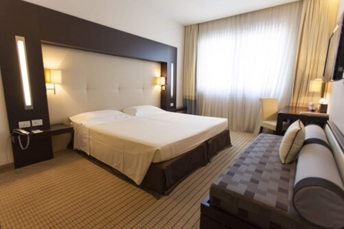 Une chambre d’hôtel avec un grand lit, des tables de chevet, un canapé et une fenêtre avec des rideaux.