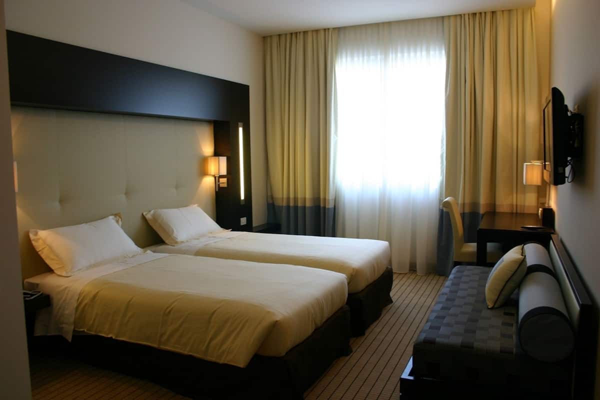Une chambre d’hôtel avec deux lits, un bureau, une chaise et un téléviseur fixé au mur.