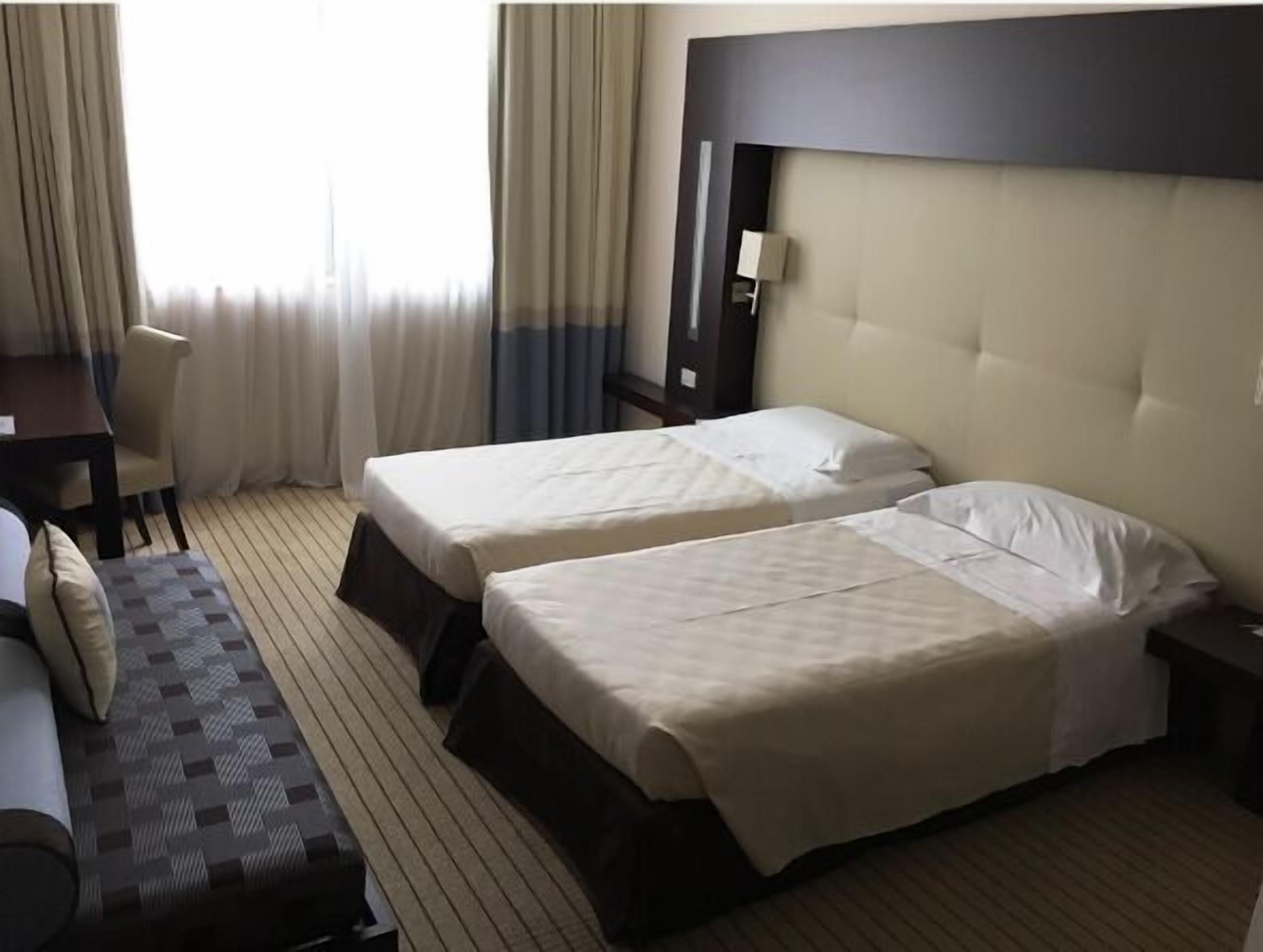 A hotel room with two beds, a desk, and a sofa.