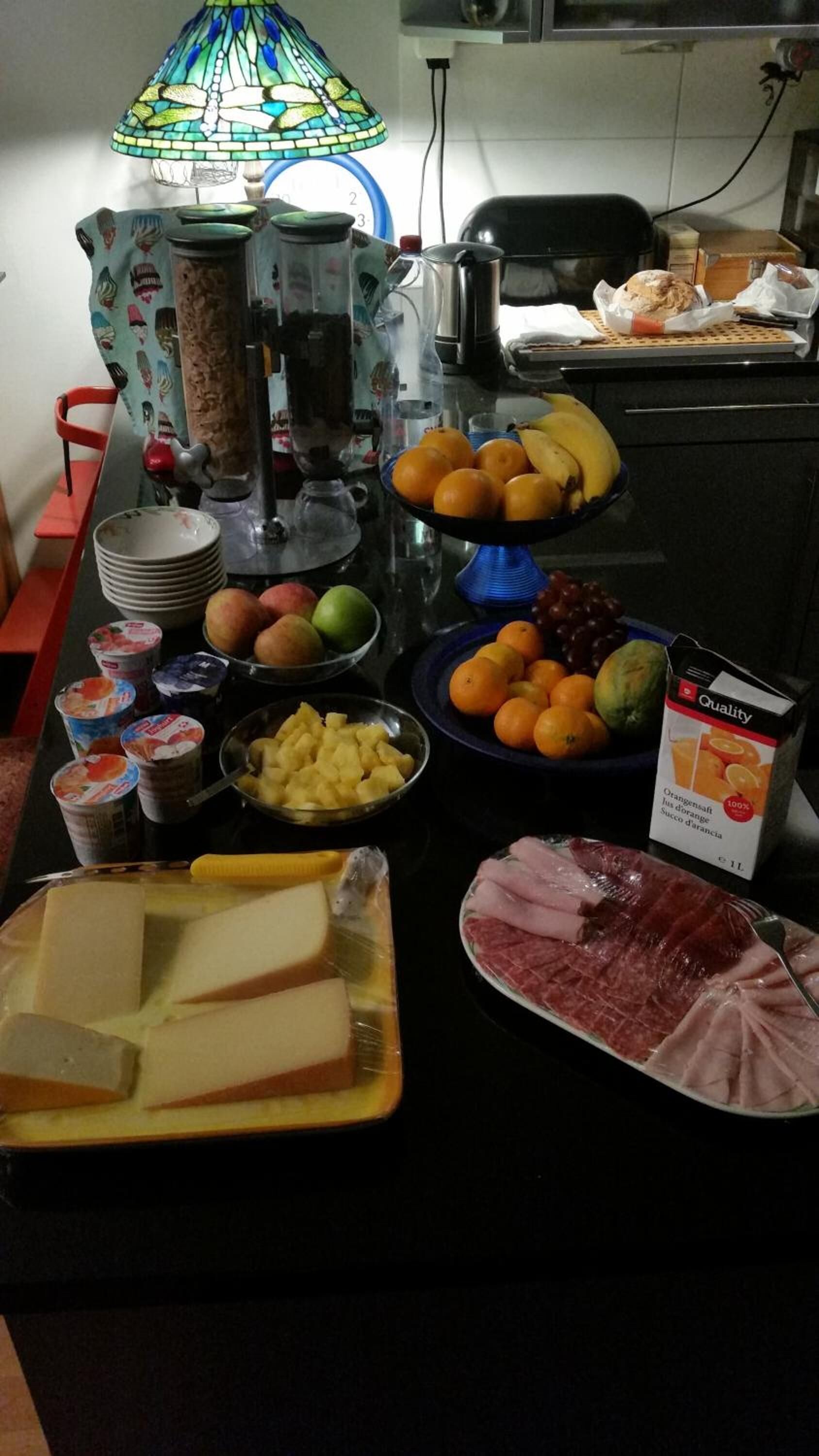 A kitchen counter with various food items, including fruits, cheese, and a carton of orange juice.