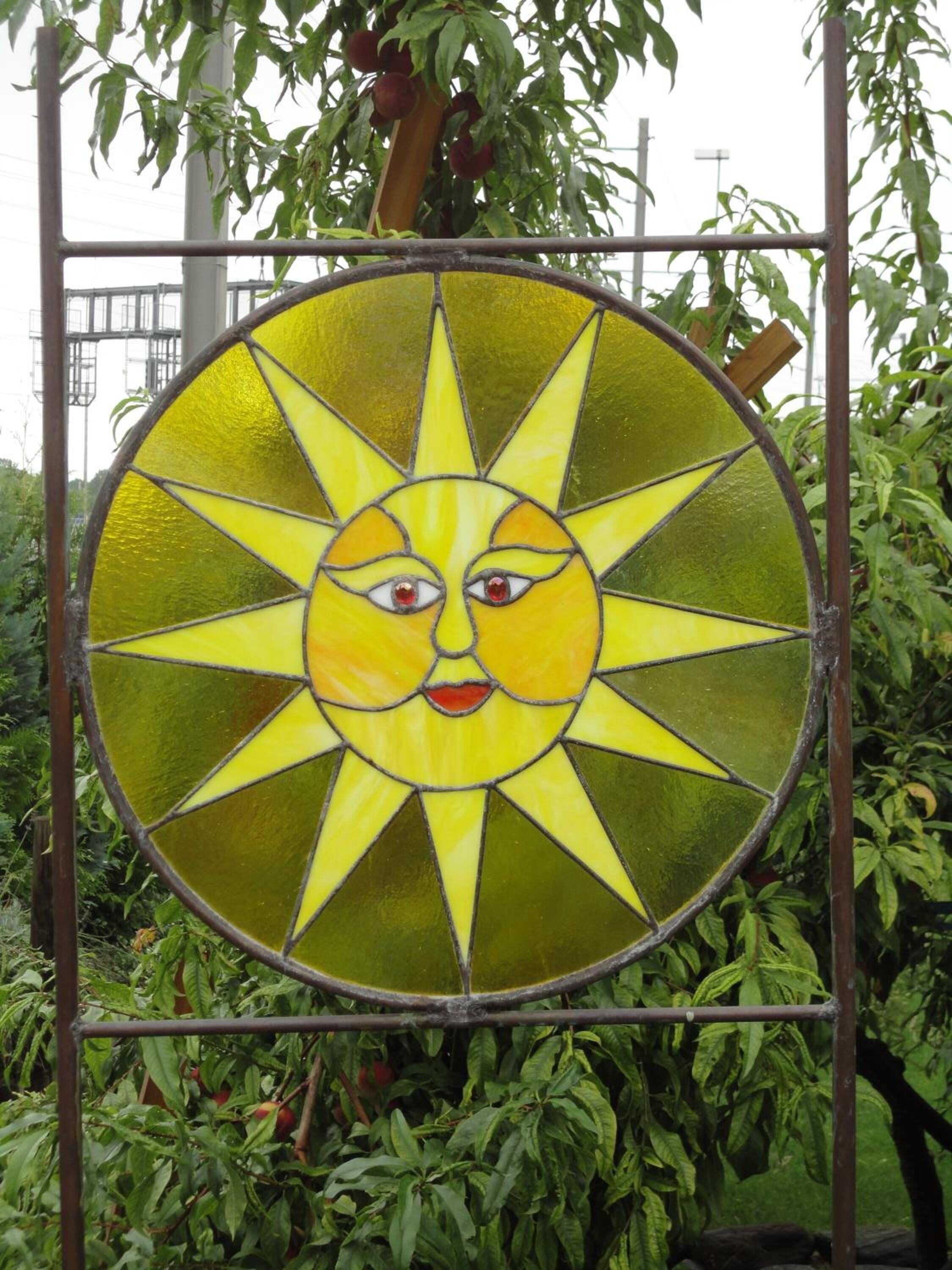 A circular stained glass artwork with a sun motif, surrounded by a metal frame.