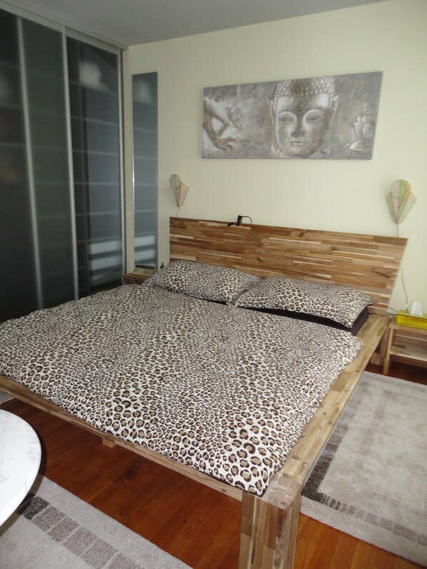 A bedroom with a wooden headboard, a bed with a leopard print bedspread, a wall-mounted artwork, and a bedside table with a lamp.