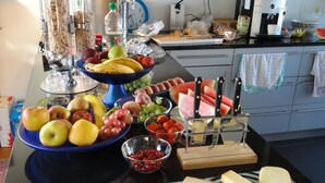 Un comptoir de cuisine sur lequel on trouve divers aliments, notamment des fruits, des fromages et un plateau de charcuterie.