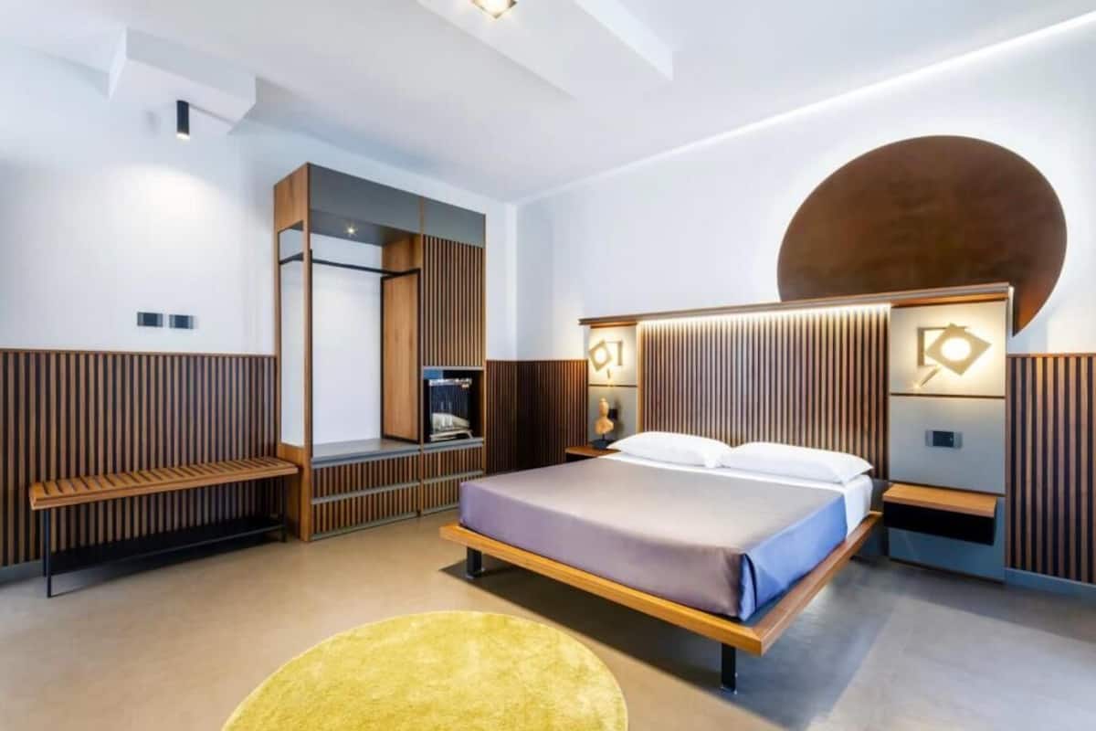 A modern bedroom with a bed, bedside tables, a bench, and a unique wall design.