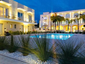 A modern hotel with a swimming pool, palm trees, and a well-lit exterior at dusk. - Vespucci Hotel (Porto Cesareo)