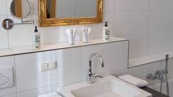 A modern bathroom with a large mirror, two sinks, a shower, and a towel rack.