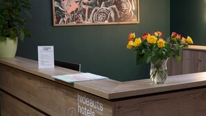 A hotel reception desk with a wooden finish, a vase of yellow and red roses, a framed artwork on the wall, and a sign with hotel information. - hideauts hotels Der Rosengarten. (Fuessen)