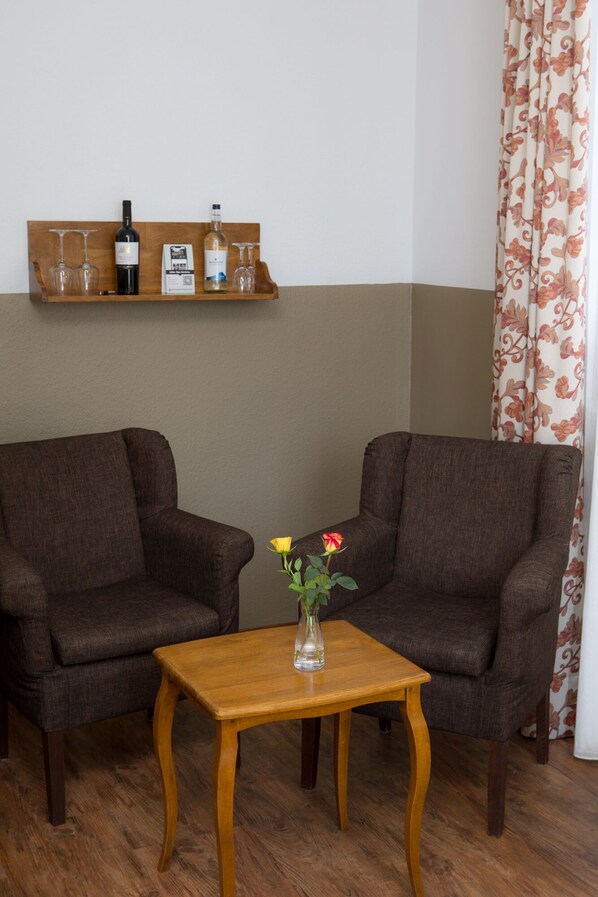 Una habitación con dos sillones marrones, una mesa de centro de madera con un florero y una estantería con botellas de vino y copas.
