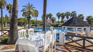 A dining area with a table set for four, overlooking a pool, surrounded by palm trees and a gazebo. - Encosta do Lago (Loulé)