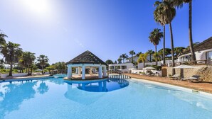 A clear blue pool with a gazebo, palm trees, and a stone building. - Encosta do Lago (Loulé)
