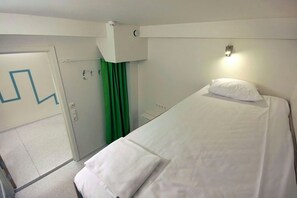 A hotel room with a single bed, a white headboard, a bedside lamp, and a green curtain. - Citysleep - Hostel (Luleå)